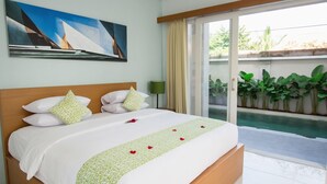 A hotel room with a bed, a painting on the wall, a green patterned bedspread, and a view of a swimming pool through a glass door. - Apple Suite Apartment (Keroboken Kelod)