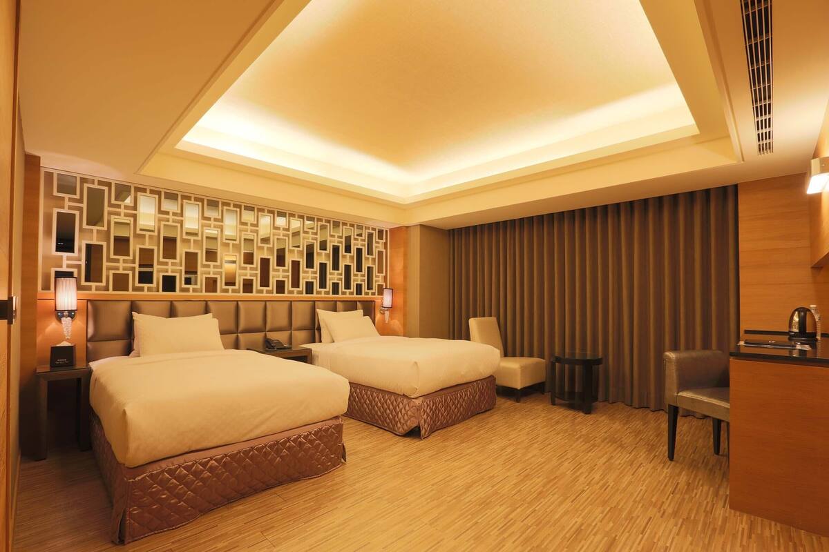 A hotel room with two beds, a desk, a chair, and a decorative wall.