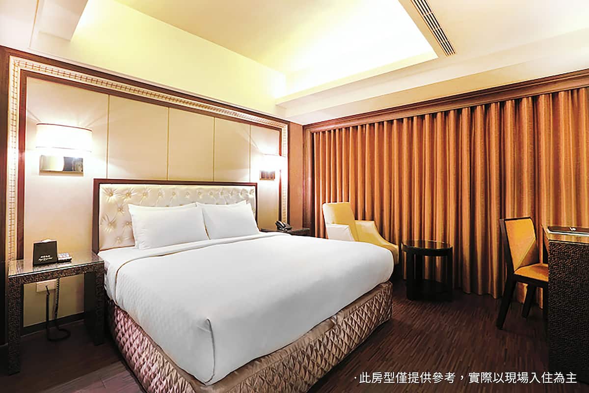 A hotel room with a large bed, a nightstand, a lamp, a chair, and a curtain.
