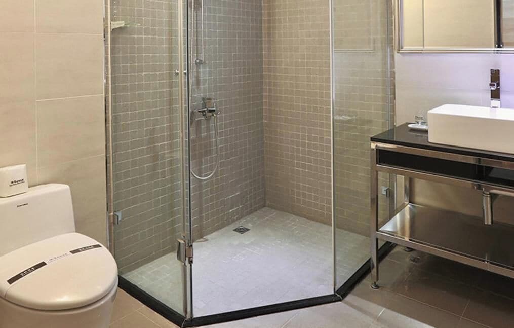Un baño con cabina de ducha de vidrio, inodoro blanco y lavamanos moderno con encimera negra.