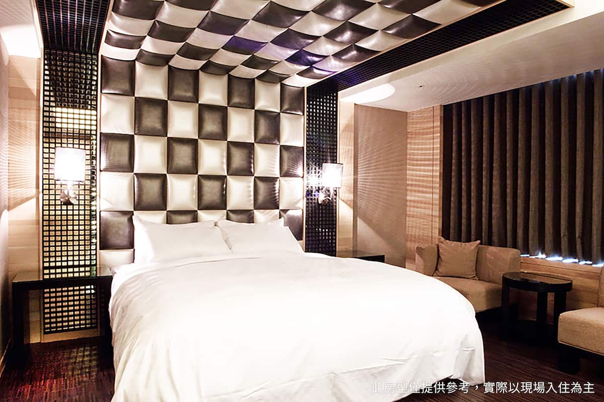 A modern hotel room with a large bed, a sofa, and a decorative wall panel.
