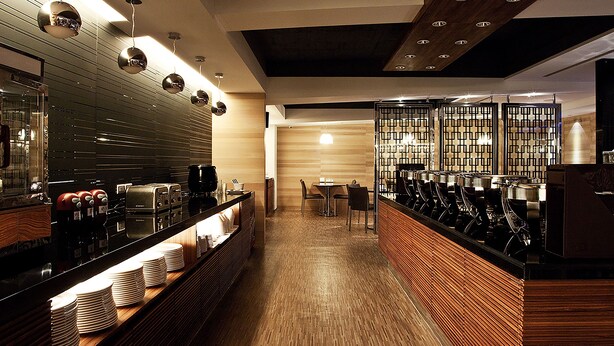 A modern bar area with a long counter, multiple coffee machines, and a seating area with tables and chairs. - Royal Group Hotel Chang Chien Branch (Kaohsiung)