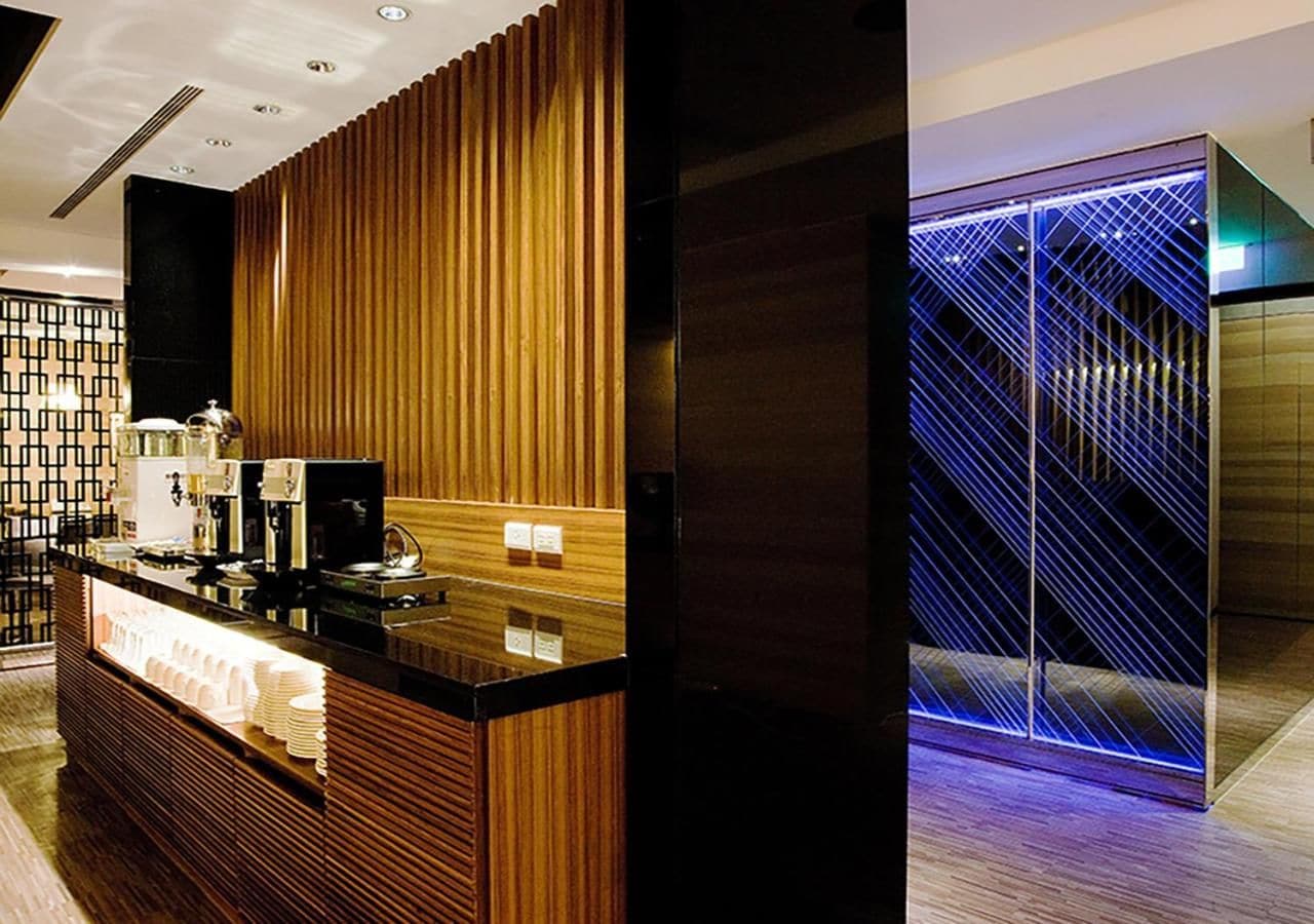 A reception area with a wooden panel design, a counter with a coffee machine, and a blue-lit elevator.