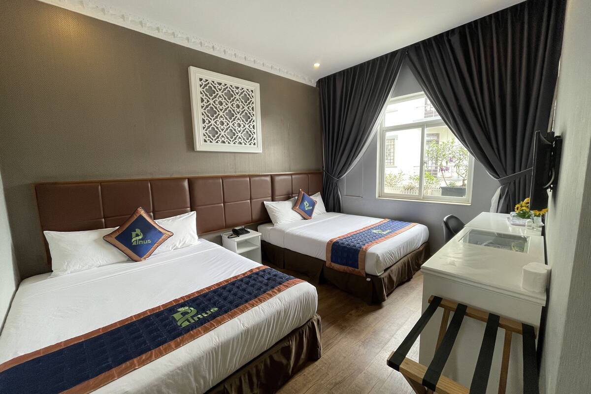 A hotel room with two beds, a desk, a chair, a window with curtains, and a decorative wall piece.