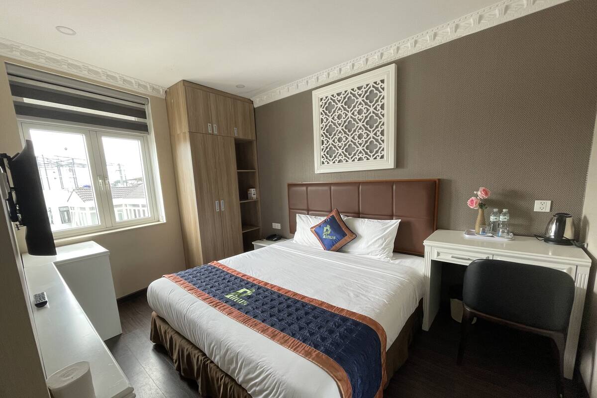 A hotel room with a large bed, a desk, a wardrobe, and a decorative wall piece.