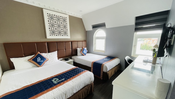 Camera d'albergo con due letti, una scrivania, una sedia, una finestra e un pannello decorativo al muro.