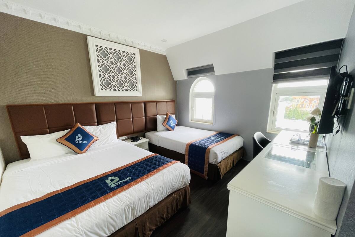 A hotel room with two beds, a desk, a chair, a window, and a decorative wall panel.