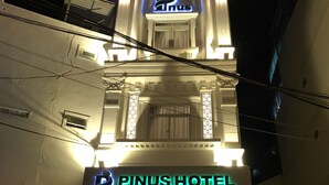 L'esterno dell'Hotel Pinus, con insegne illuminate e uno stile architettonico classico.