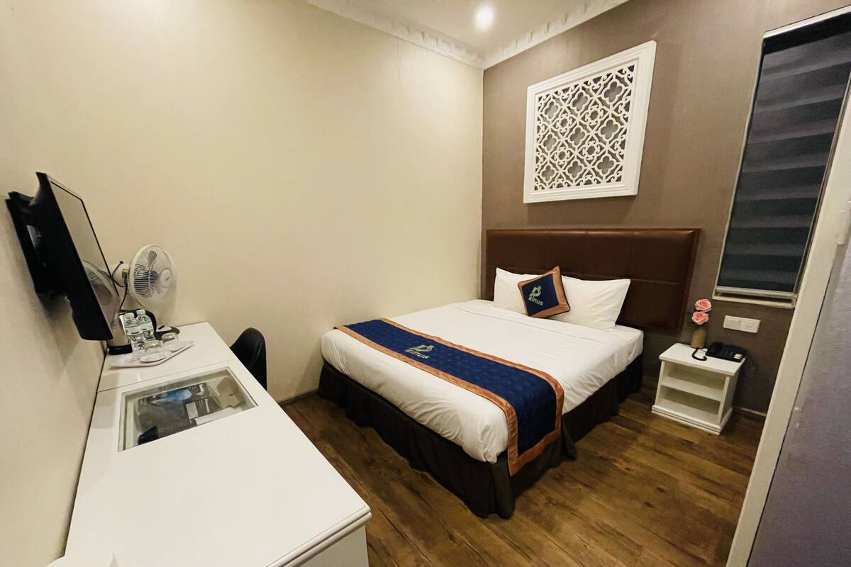A hotel room with a bed, bedside table, desk, mirror, and a decorative wall panel.