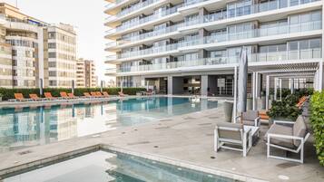 A modern hotel with a swimming pool, outdoor seating, and a covered area.