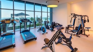 Ett gym med löpband, motionscyklar och styrketräningsmaskiner, stora fönster och utsikt över havet.