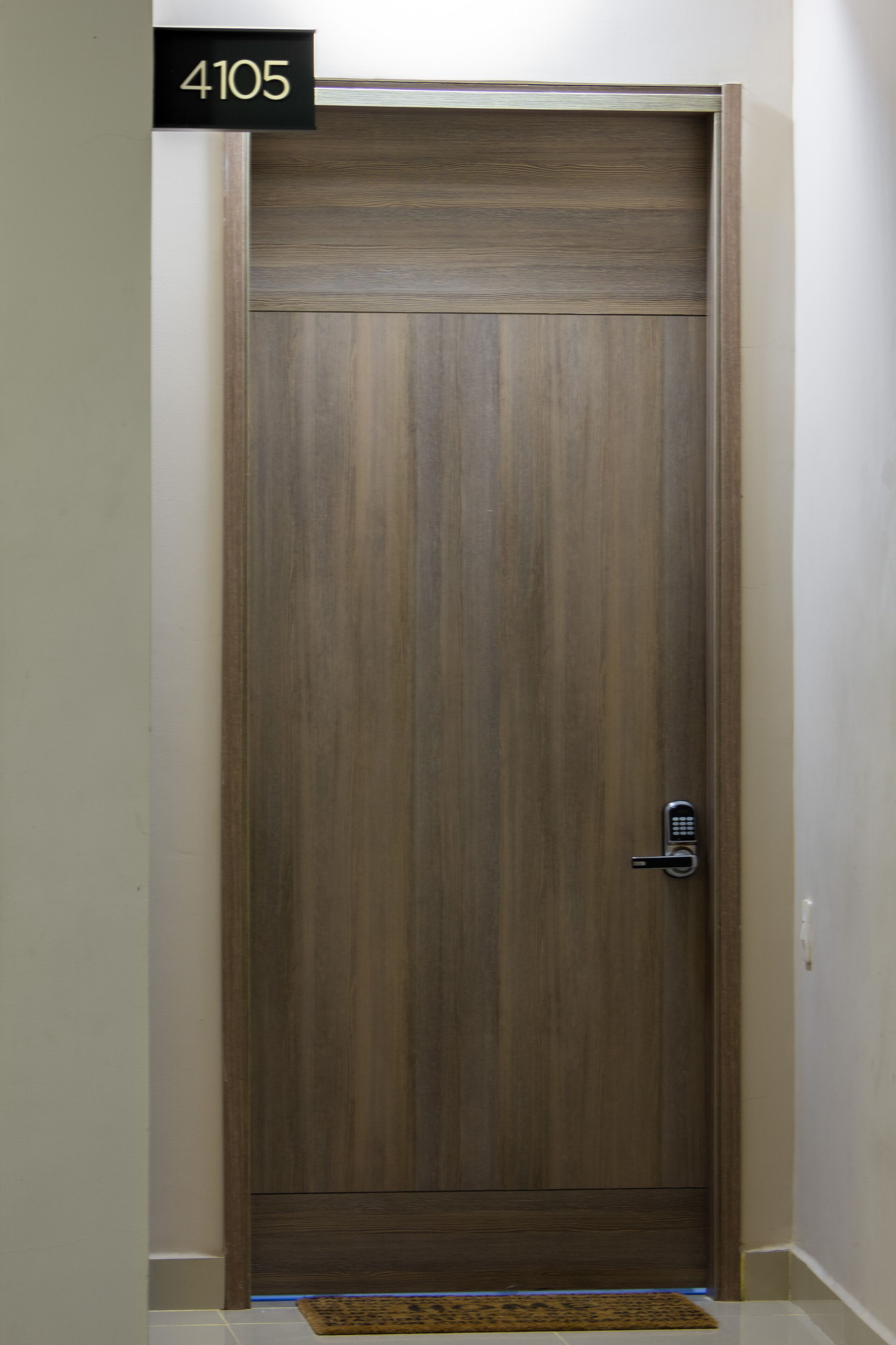 A wooden door with a keypad lock, a number plate above it, and a doormat at the base.