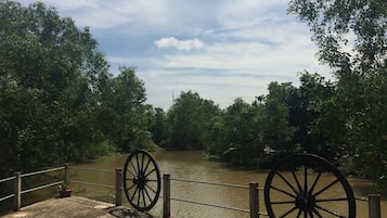 A riverside walkway with a wooden fence and two large wheels, surrounded by dense greenery.