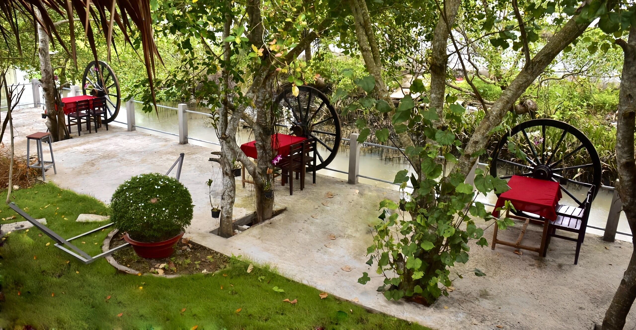 Un espace extérieur aménagé en terrasse, avec des tables et des chaises, entouré d’arbres et de verdure.