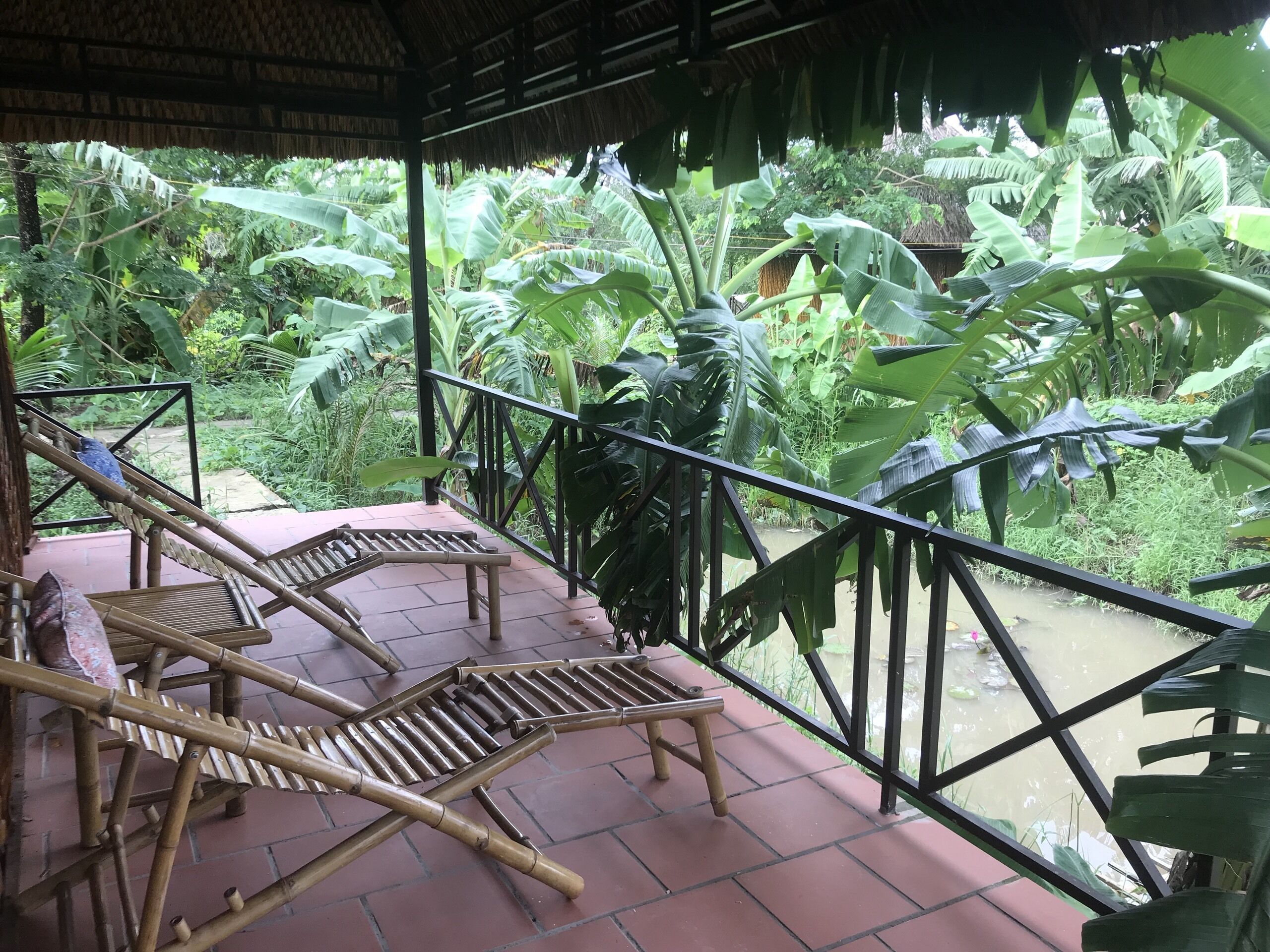 Un área de estar al aire libre cubierta con mobiliario de bambú, rodeada de exuberante vegetación tropical.
