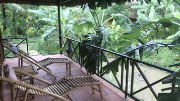 Un área de estar al aire libre cubierta con mobiliario de bambú, rodeada de exuberante vegetación tropical.