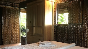 Quarto com cama, porta de madeira, espelho e ventilador.