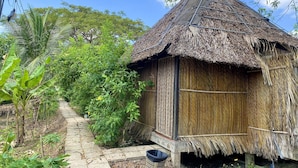 Uma cabana com telhado de palha e um caminho de pedra que a leva, rodeada por vegetação exuberante.