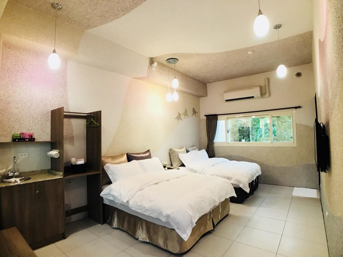 A hotel room with two beds, a bathroom, a sink, and a window with a view of greenery.