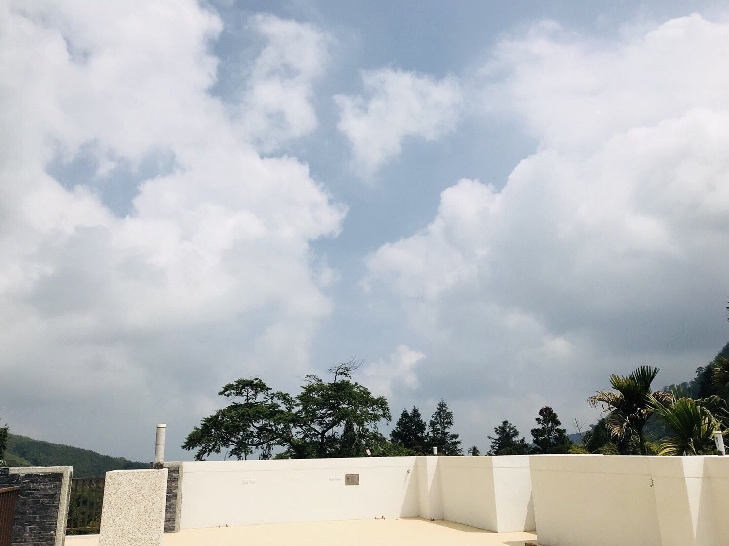 Un tetto con un muro bianco e un camino, circondato da alberi e un cielo sereno.