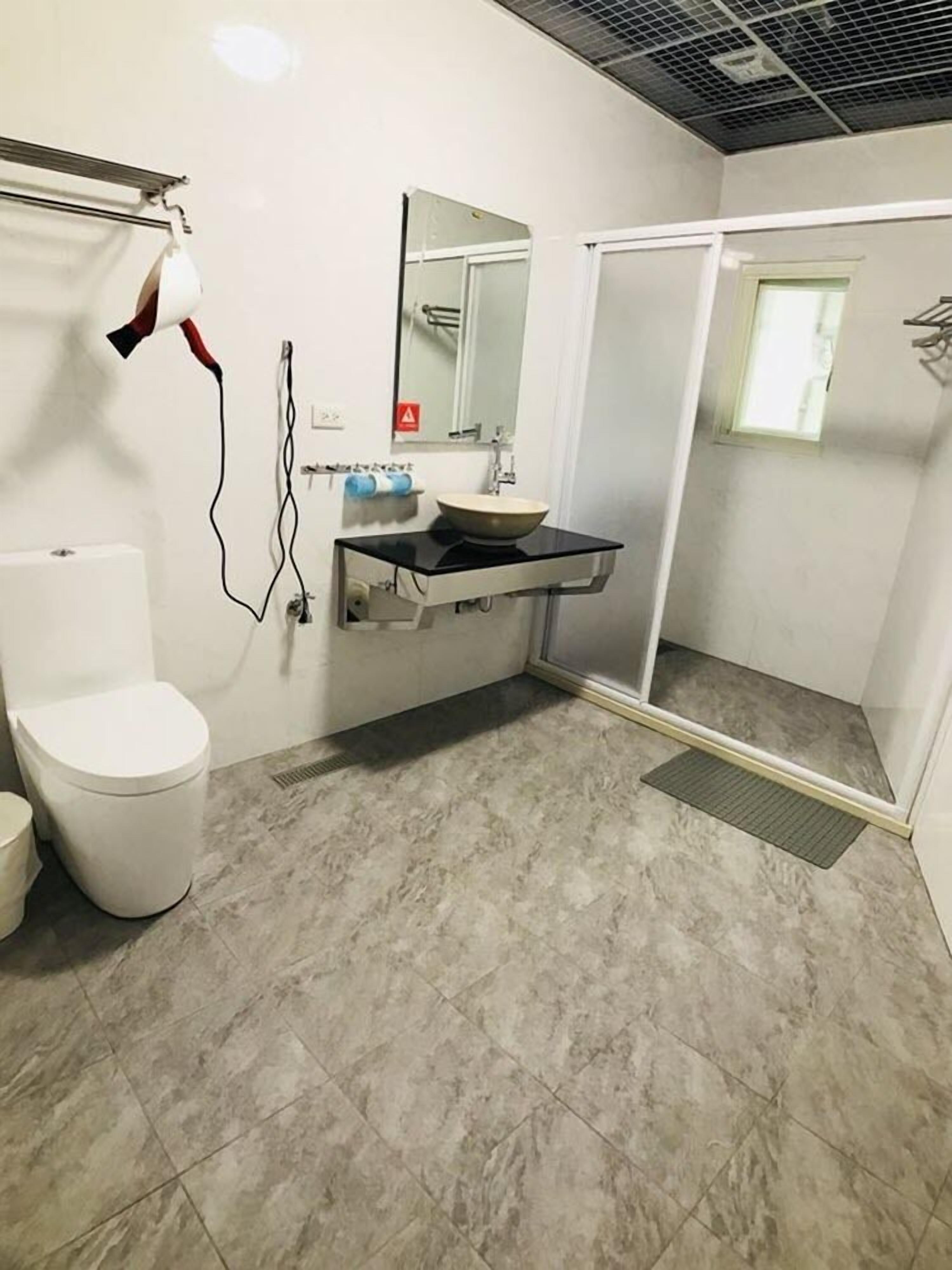 Une salle de bain avec des toilettes blanches, un lavabo avec un miroir et un espace douche.