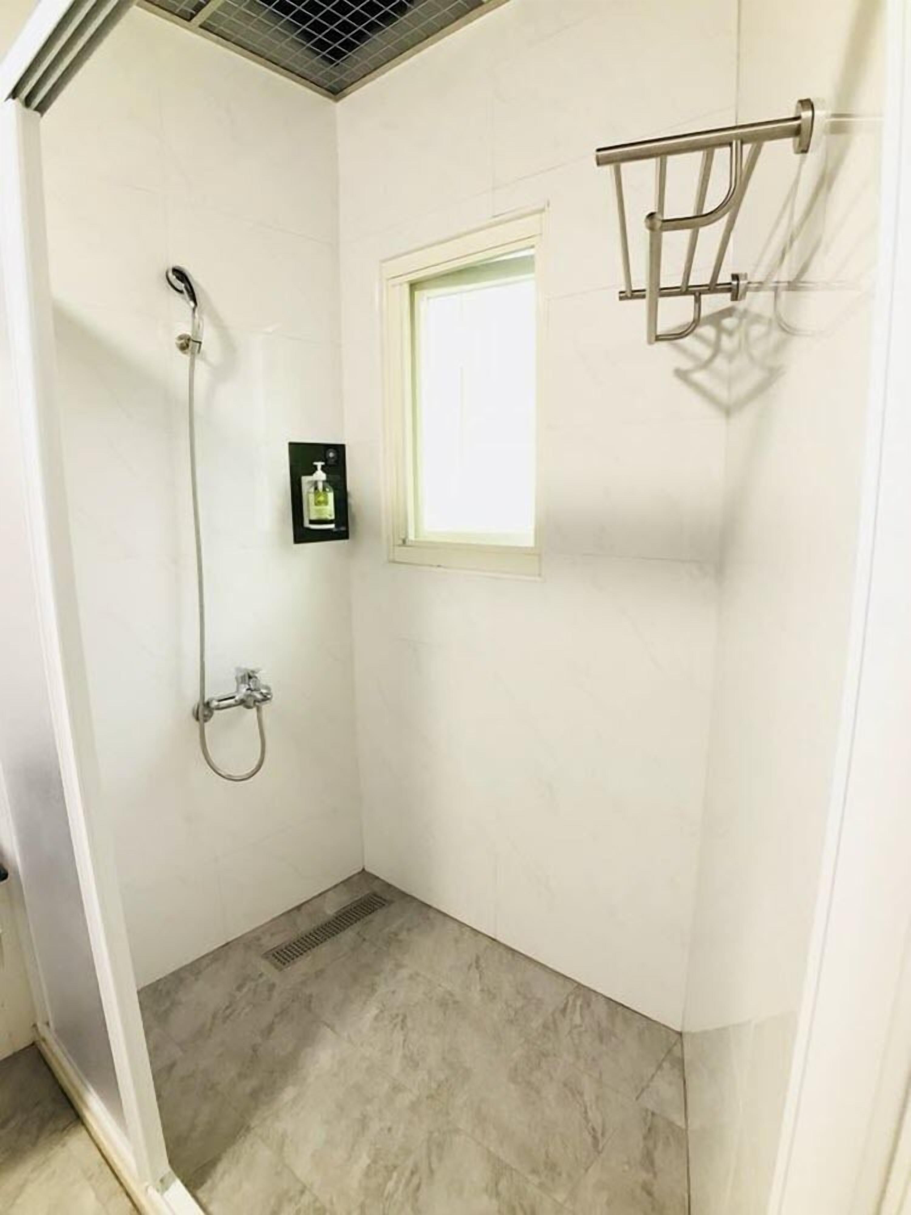 A small, white bathroom with a shower, a window, and a soap dispenser.