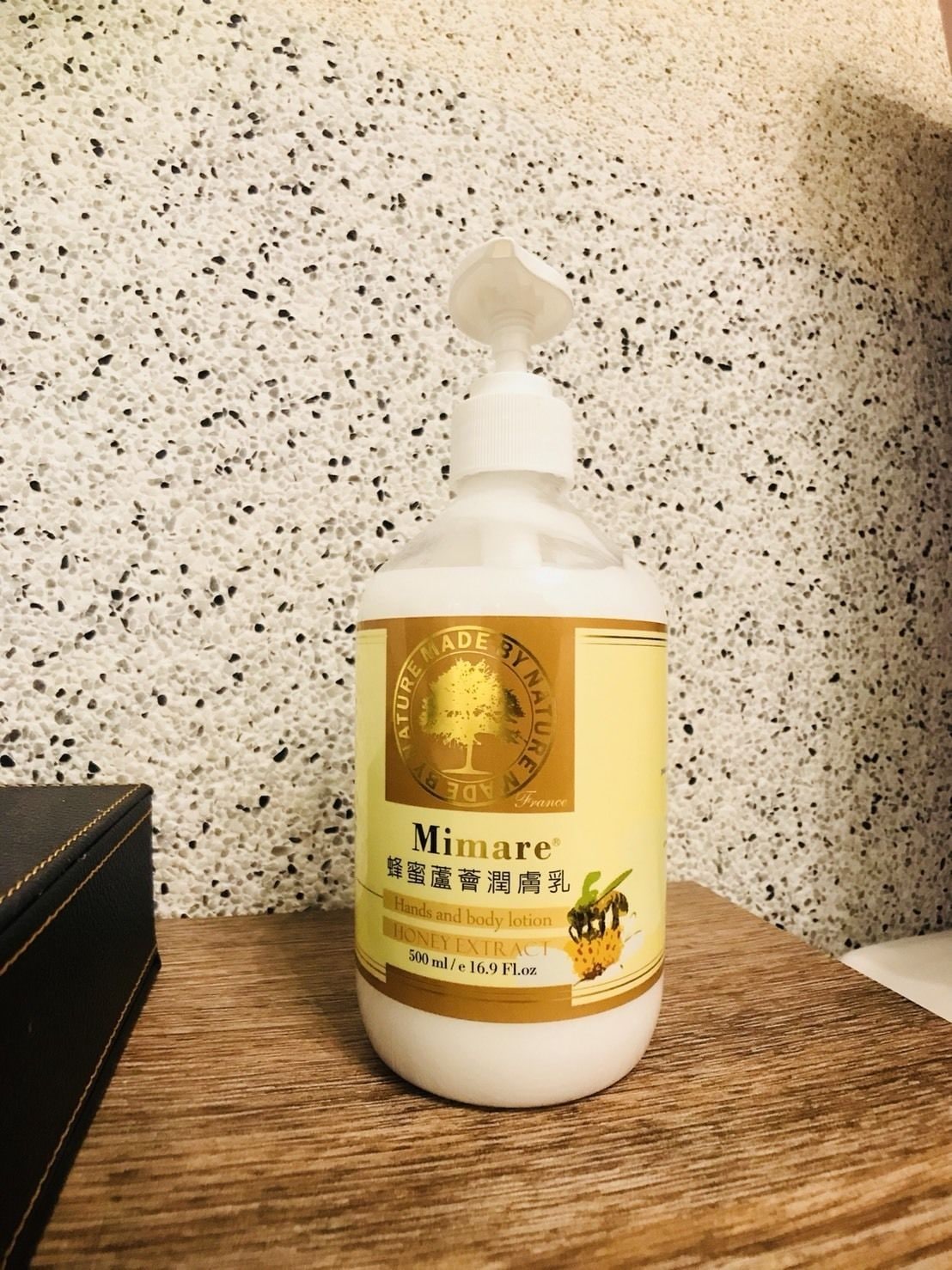 A bottle of Mimare lotion on a wooden surface against a speckled wall.