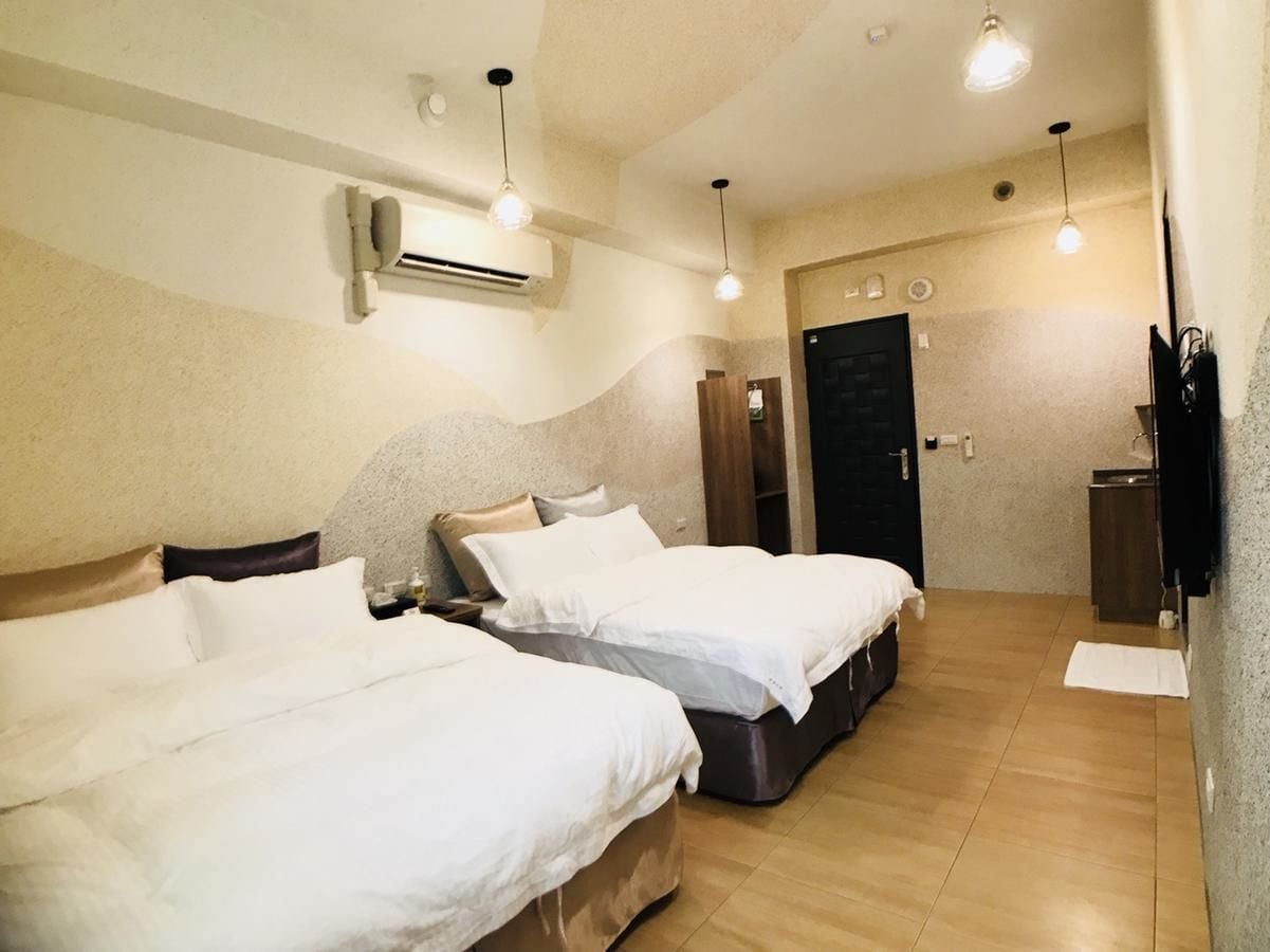 A hotel room with two beds, a wooden floor, an air conditioning unit, and a door leading to a bathroom.