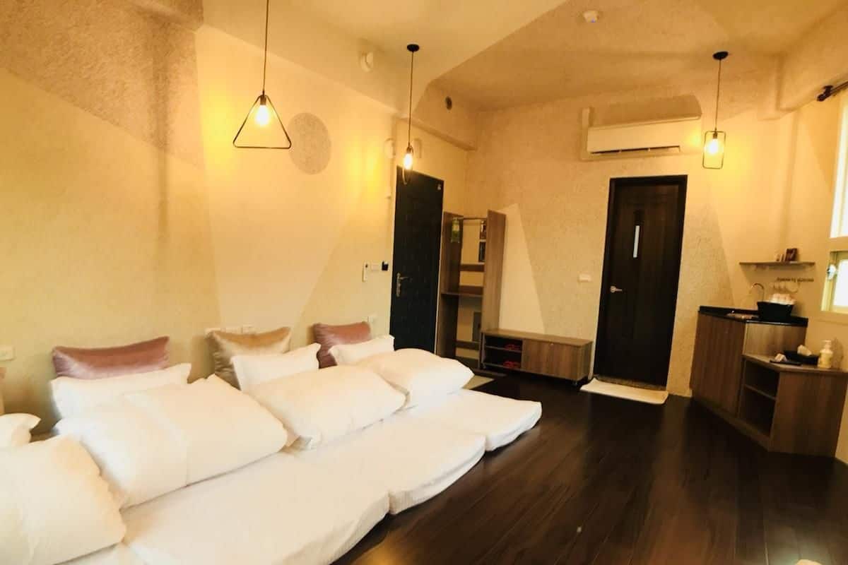 Habitació amb un llit gran, un sòl de fusta, una cuineta petita i una porta que condueix a una altra habitació.