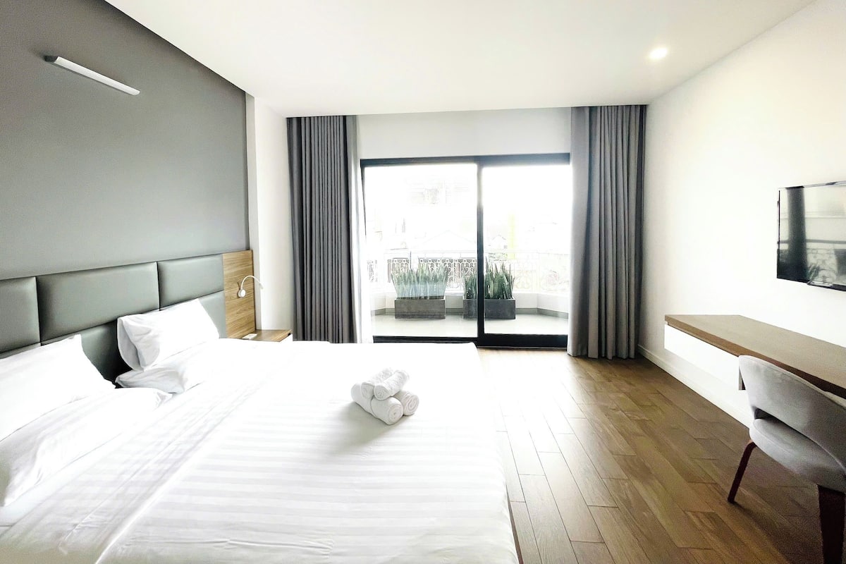 A hotel room with a large bed, a desk, and a view of the outside.
