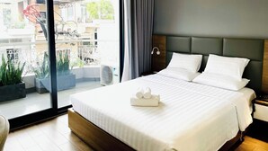 Habitación de hotel con una cama grande, una mesita de noche, un cabecero moderno, un ventanal con vistas al exterior y una planta en maceta.
