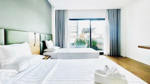 Habitación de hotel con dos camas, un ventanal con cortinas y vistas a edificios.