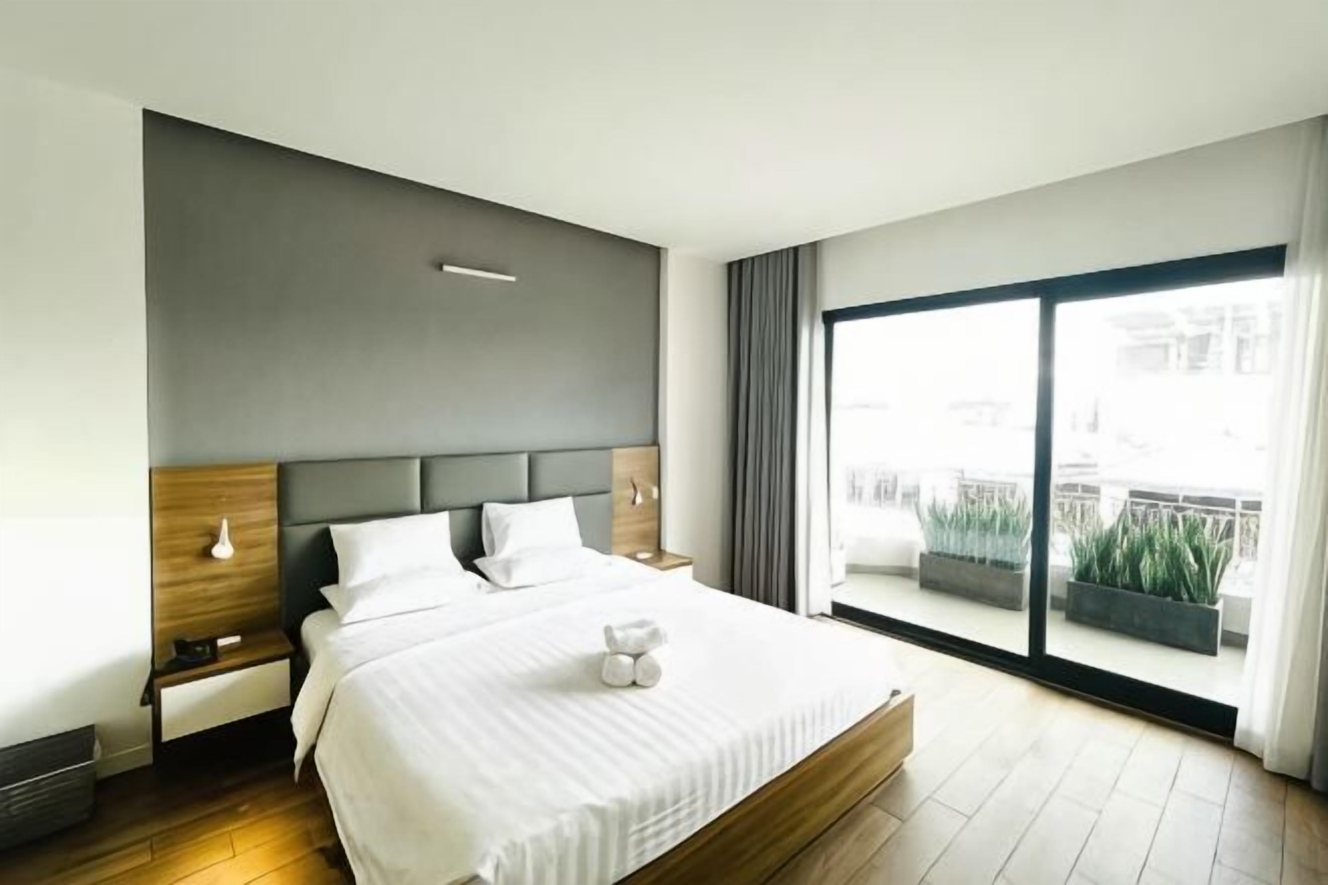 Ein modernes Hotelzimmer mit einem großen Bett, einem Nachttisch, einem Fenster mit Blick auf die Stadt und einem Balkon mit Pflanzen.