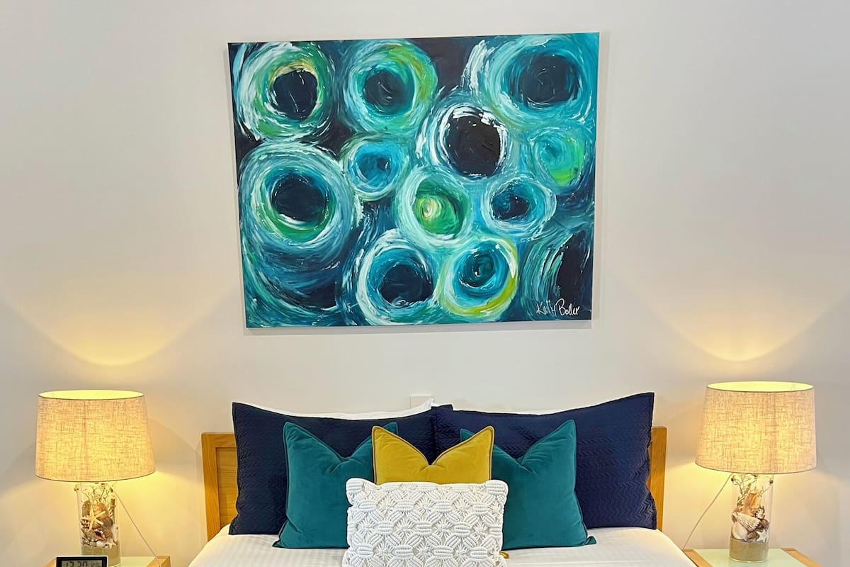 Une chambre à coucher avec un lit, deux tables de chevet, un tableau accroché au mur et une horloge.