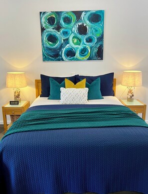 A bedroom with a bed, two bedside tables, a wall-mounted painting, and a clock. - Coastal Waters Motor Inn (Lakes Entrance)