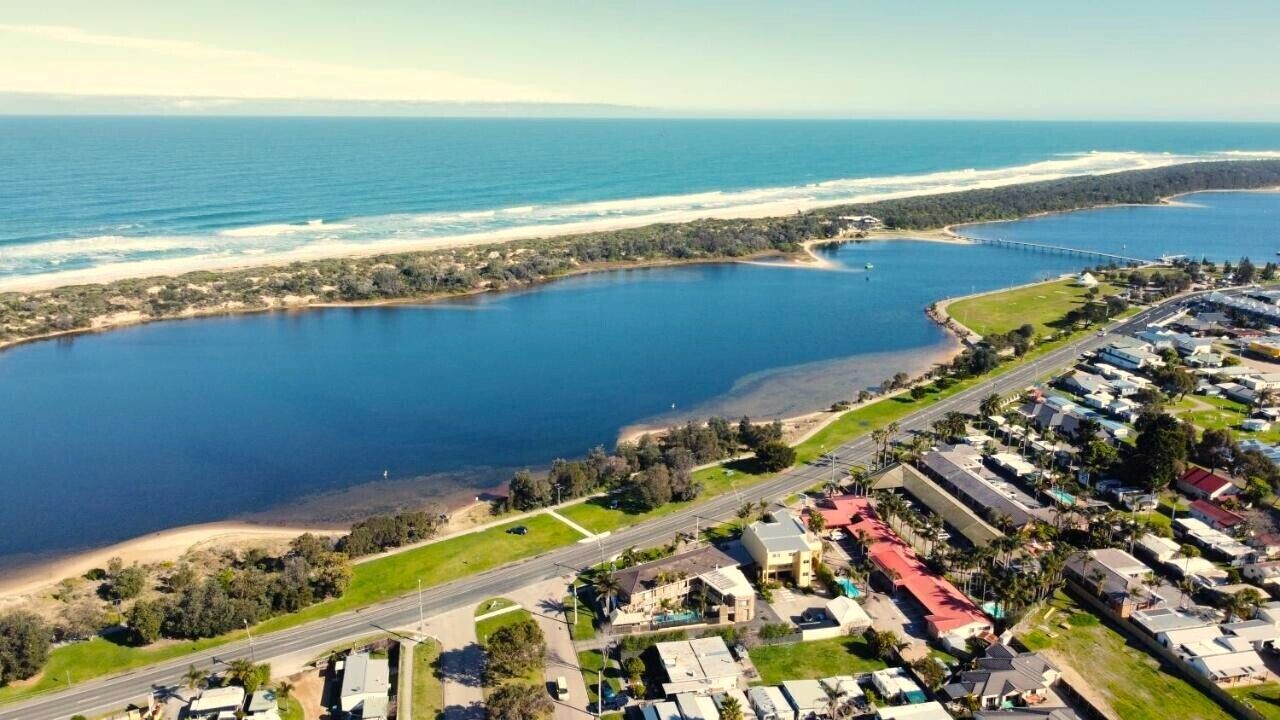 Une vue aérienne d’une zone côtière comprenant une étendue d’eau importante, un pont et une zone résidentielle avec des maisons et des routes.