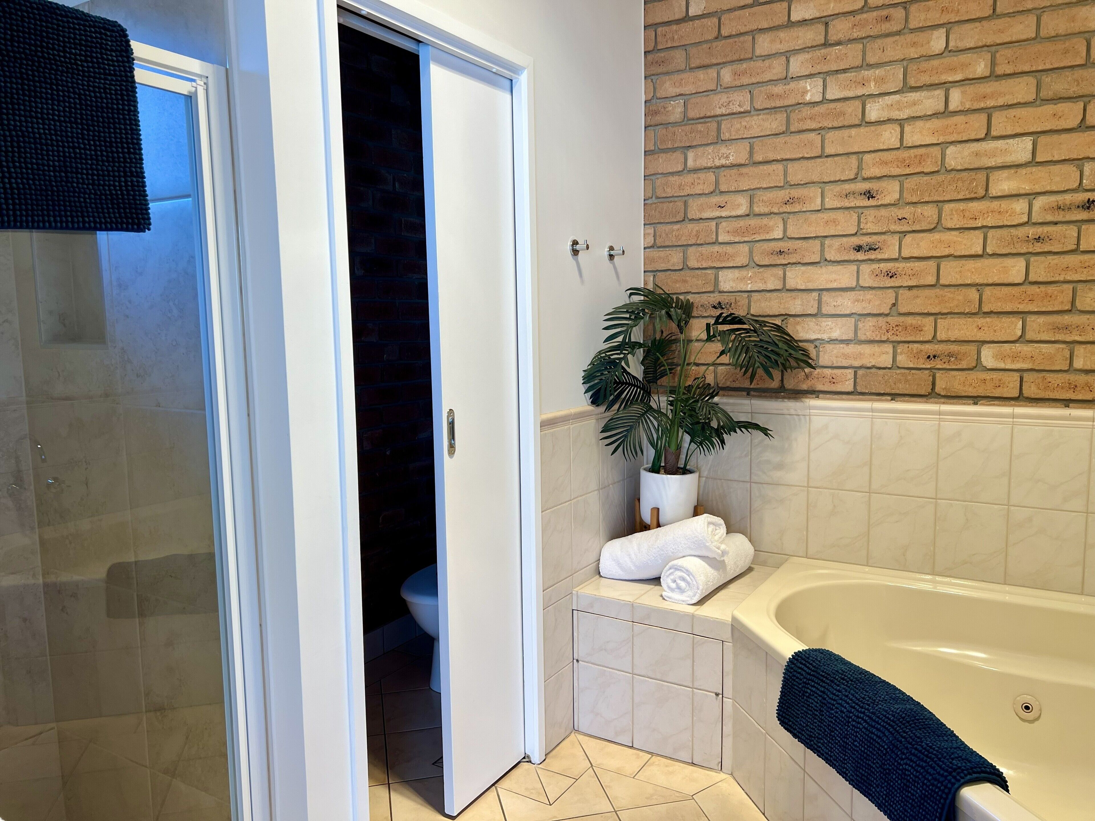 A bathroom with a bathtub, a potted plant, and a towel on a small stool.