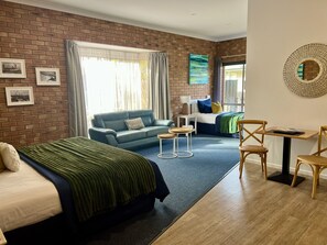 A room with a brick wall, a bed, a sofa, a small table, and a chair. - Coastal Waters Motor Inn (Lakes Entrance)