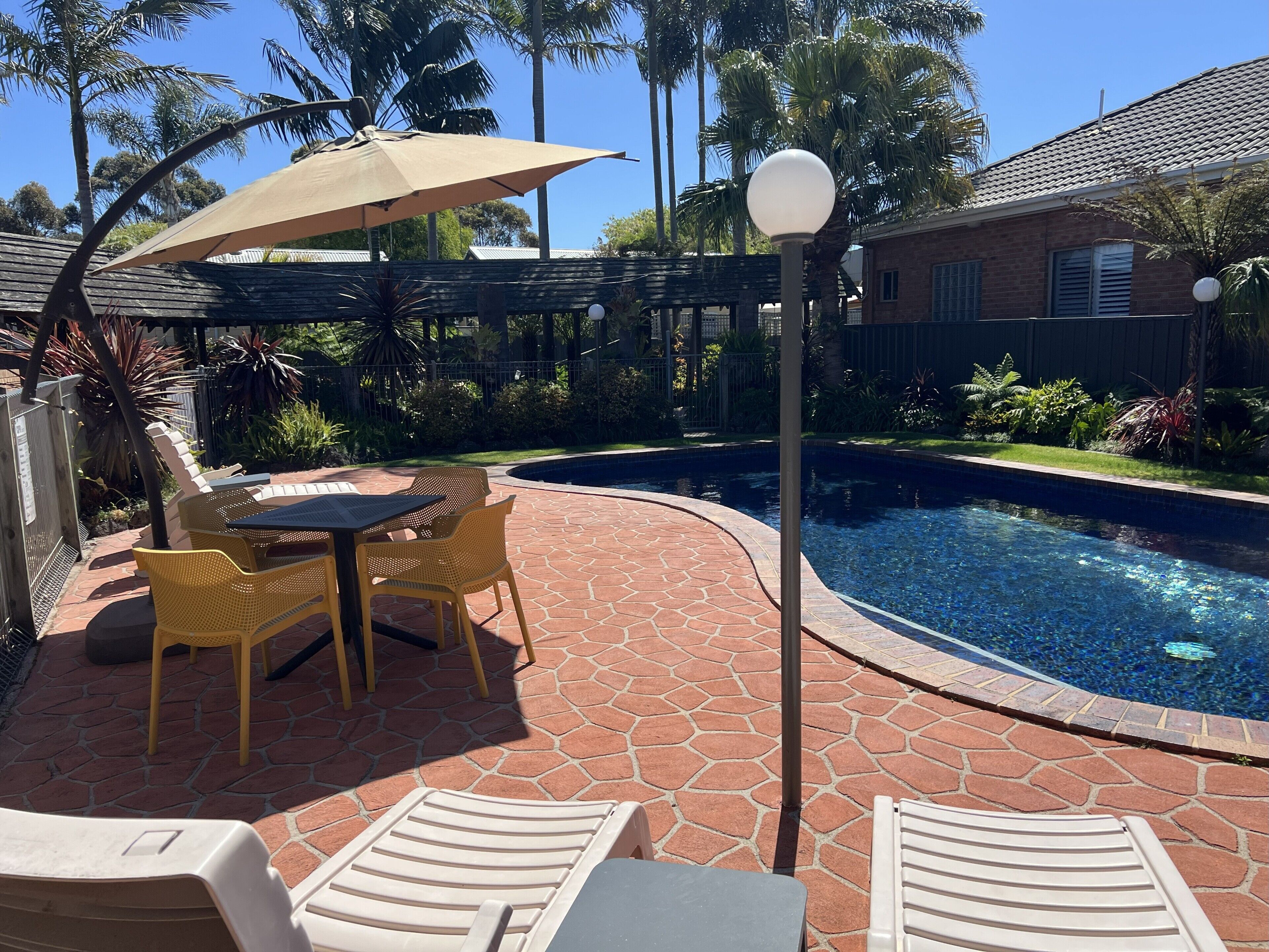 A poolside area with a table and chairs, a pergola with an umbrella, and a lamp post.