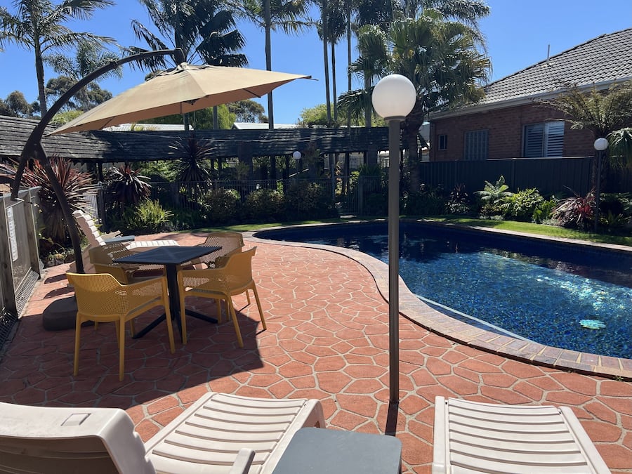 Et poolområde med et bord og stole, en pergola med parasol og en lygtepæl.