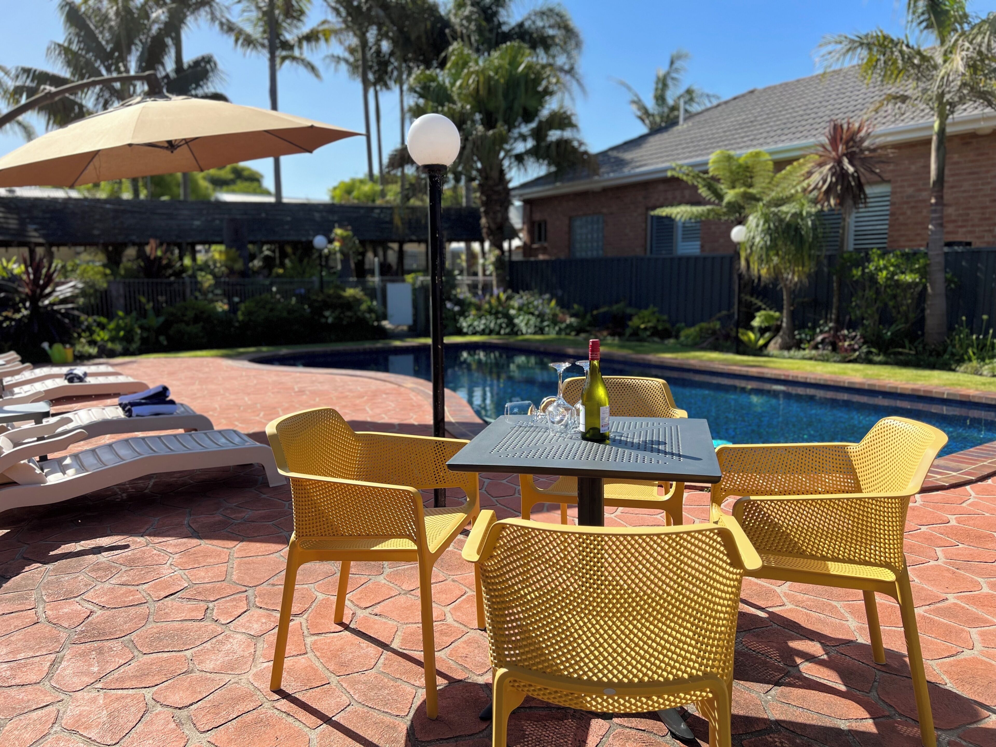 Un espace aménagé au bord de la piscine avec des chaises jaunes, une table et une bouteille de vin.