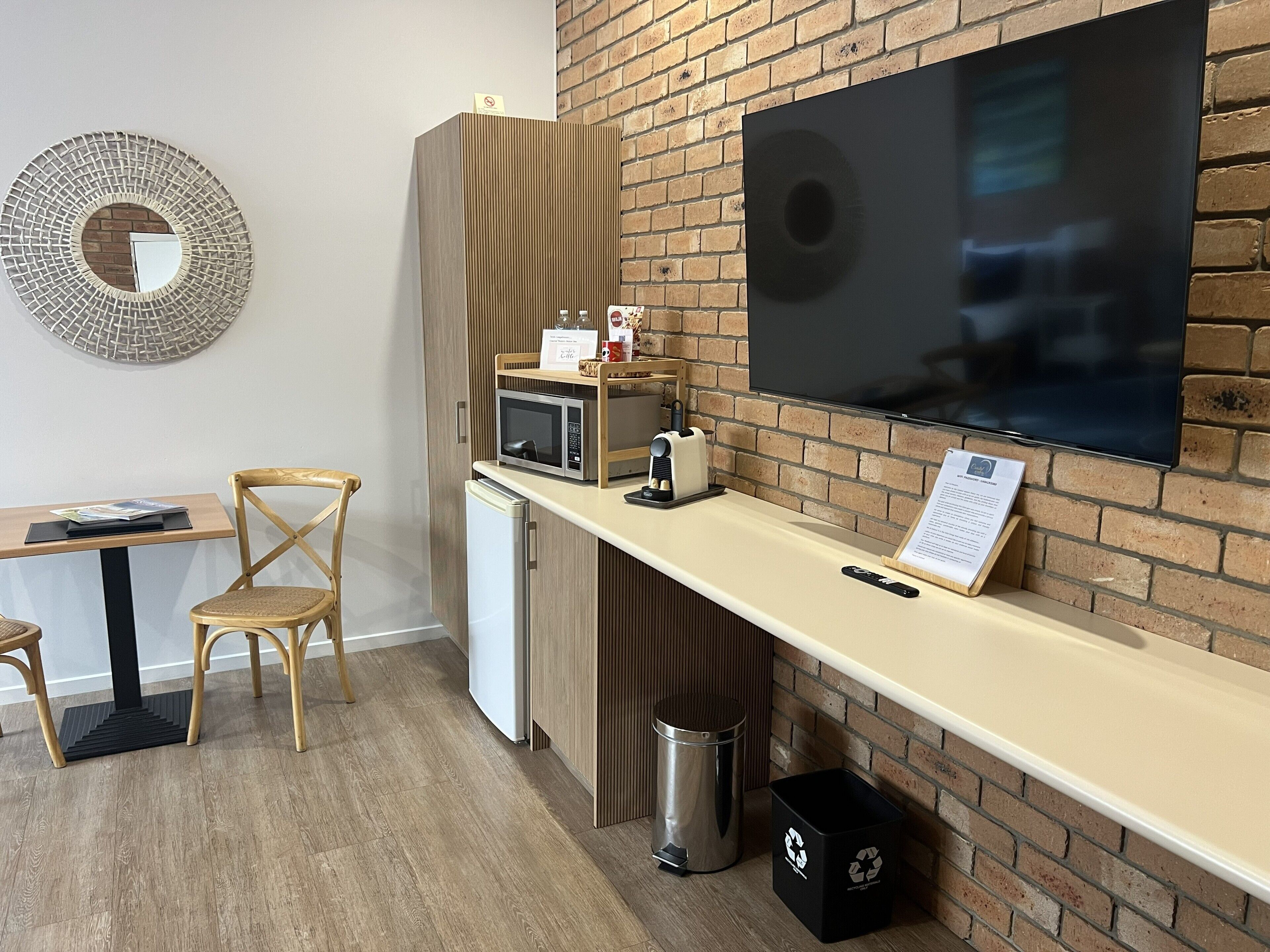 A kitchenette with a microwave, toaster, and a TV mounted on a brick wall.