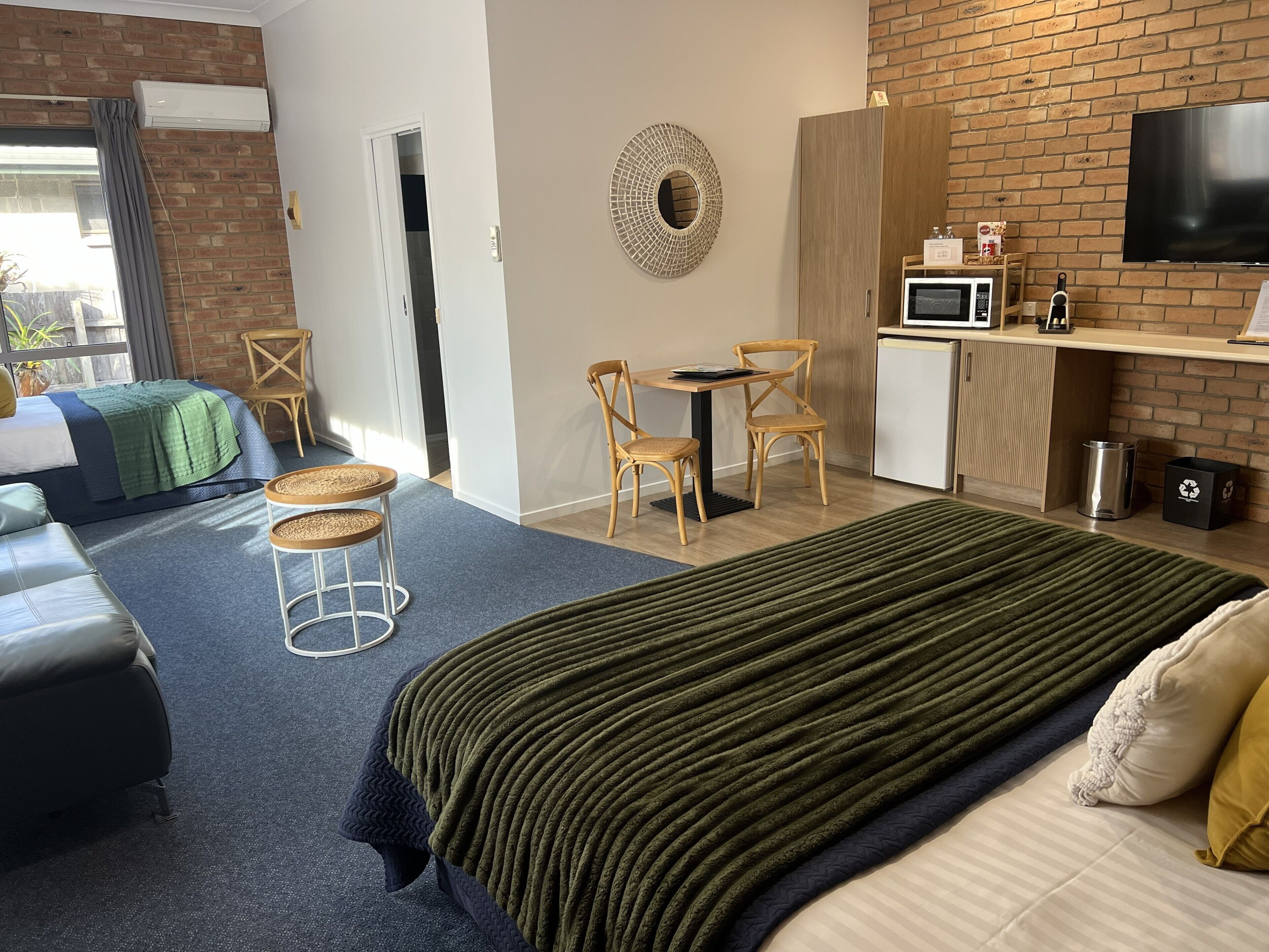 Et hotelværelse med en seng, to stole, et lille bord, en mikrobølgeovn, et fjernsyn og en murstensvæg.