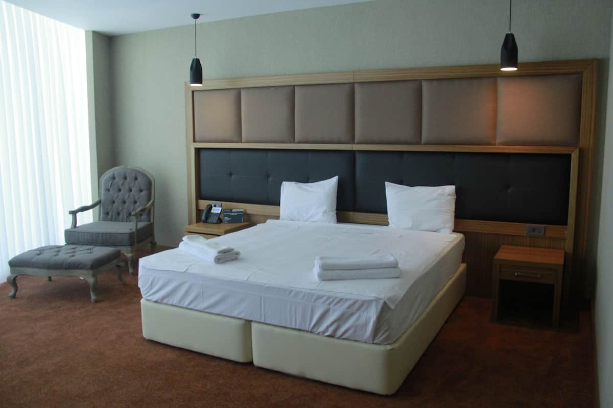 A hotel room with a large bed, a chair, a bedside table, and a nightstand.