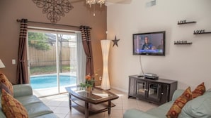 A living room with a glass-top coffee table, two sofas, a TV, and a pool visible through the sliding glass door. - Ly53820 - Indian Ridge - 3 Bed 2 Baths Villa (Kissimmee)