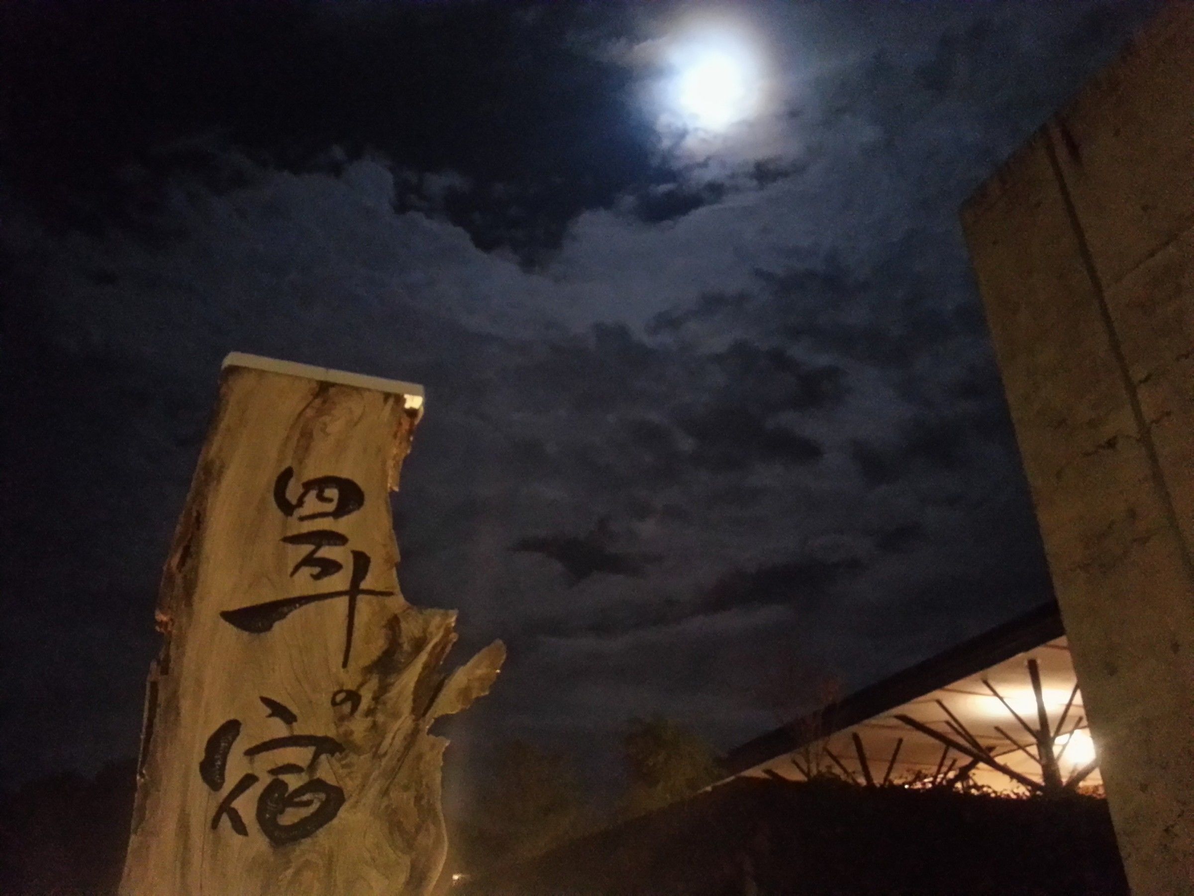 A wooden sign with Chinese characters, a moon in the sky, and a concrete structure in the background.