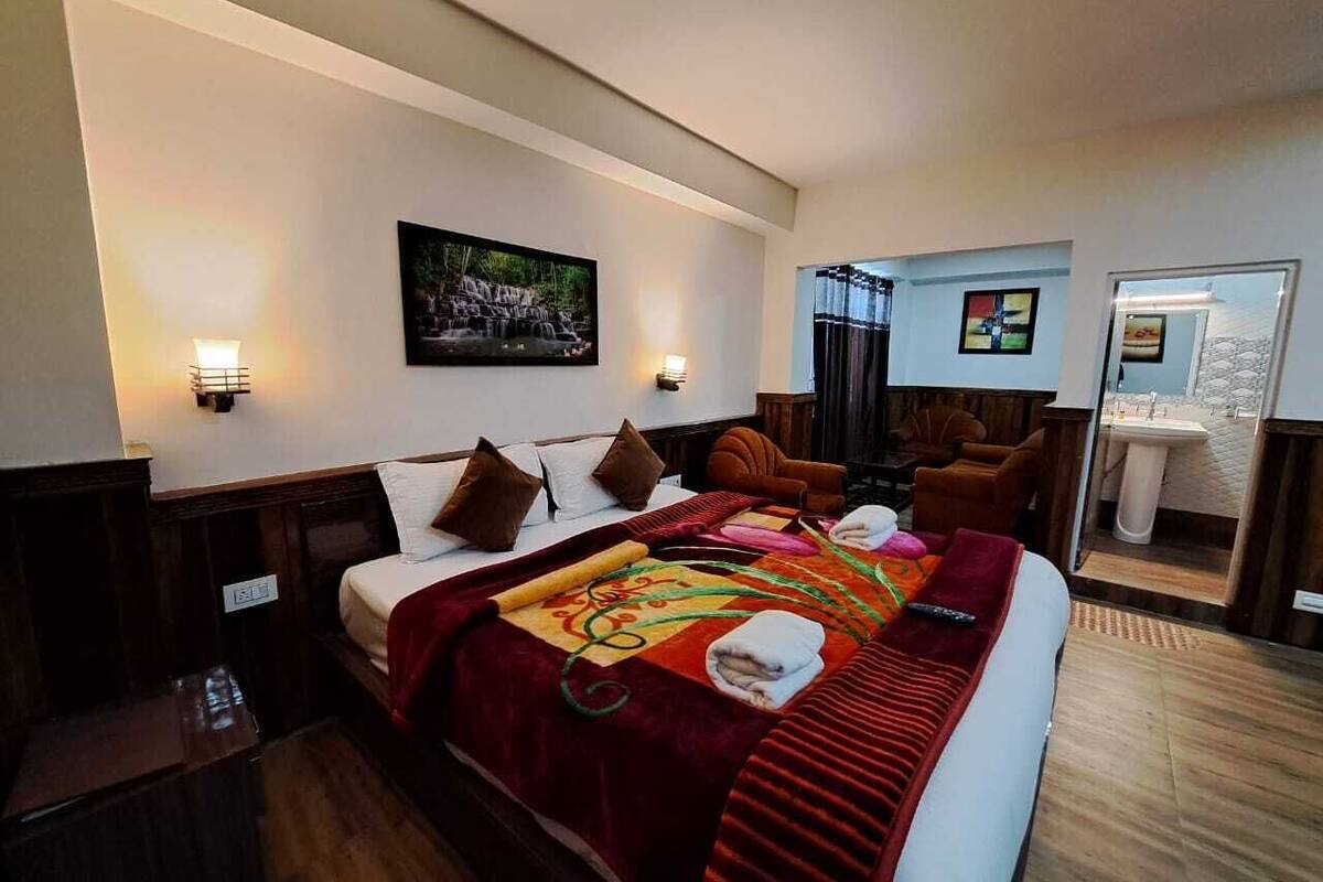 A hotel room with a large bed, a wooden headboard, a red blanket, and a painting on the wall.