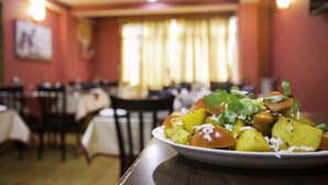 Uma sala de jantar com mesas e cadeiras, um prato de comida sobre a mesa e uma janela com cortinas.