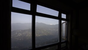 Vista pela janela, com padrão quadriculado, para uma paisagem montanhosa com luzes dispersas.
