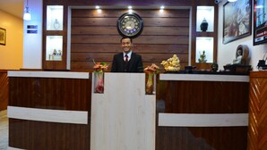Balcão de recepção com um relógio acima, painéis de madeira nas paredes e diversas estátuas e decorações no balcão.
